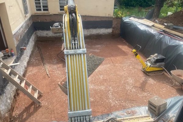 Bagger bei Erdarbeiten in Baugrube vor Bestandsgebäude – Vorbereitung für Fundament durch Dahl Bau