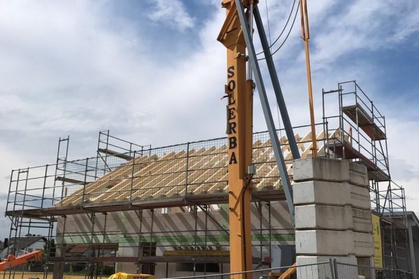Baukran vor eingerüstetem Rohbau mit aufgesetztem Dachstuhl – Baustellenarbeit von Dahl Bau