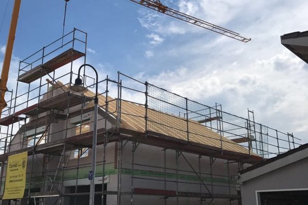 Neubau mit Gerüst und montiertem Dachstuhl, daneben ein Baukran – Baustelle von Dahl Bau