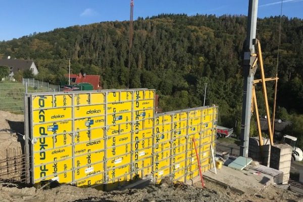 Gelbe Doka-Wandschalung am Hang mit Baukran im Hintergrund – Höhenbaustelle von Dahl Bau
