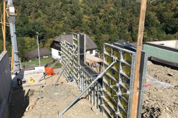 Seitlich abgestützte Doka-Schalung an Hangbaustelle mit Blick ins Tal – Stützwandvorbereitung bei Dahl Bau