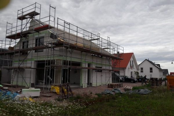 Haus im Rohbau mit Baugerüst, grünem Dämmmaterial und Arbeitsmaterialien – Neubauprojekt mit Dahl Bau