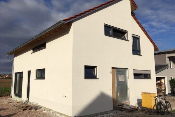 Frisch verputztes Einfamilienhaus mit Satteldach und dunklen Fenstern – Neubauprojekt in der finalen Bauphase