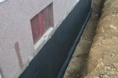 Schwarze Abdichtungsschicht entlang eines Fundaments mit Erdreich – Feuchtigkeitsschutz bei Dahl Bau